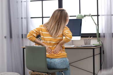 Photo of Young woman suffering from back pain in office