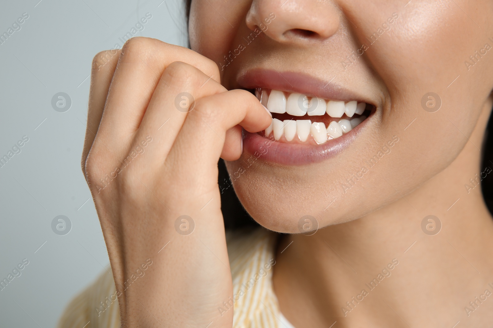 Photo of Young woman biting her nails on light grey background, closeup
