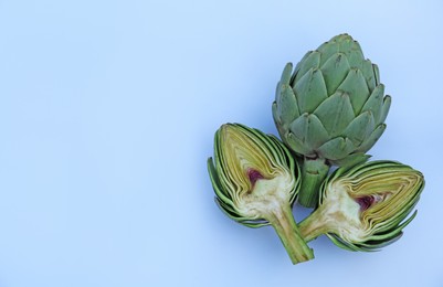 Photo of Cut and whole fresh raw artichokes on light blue background, flat lay. Space for text