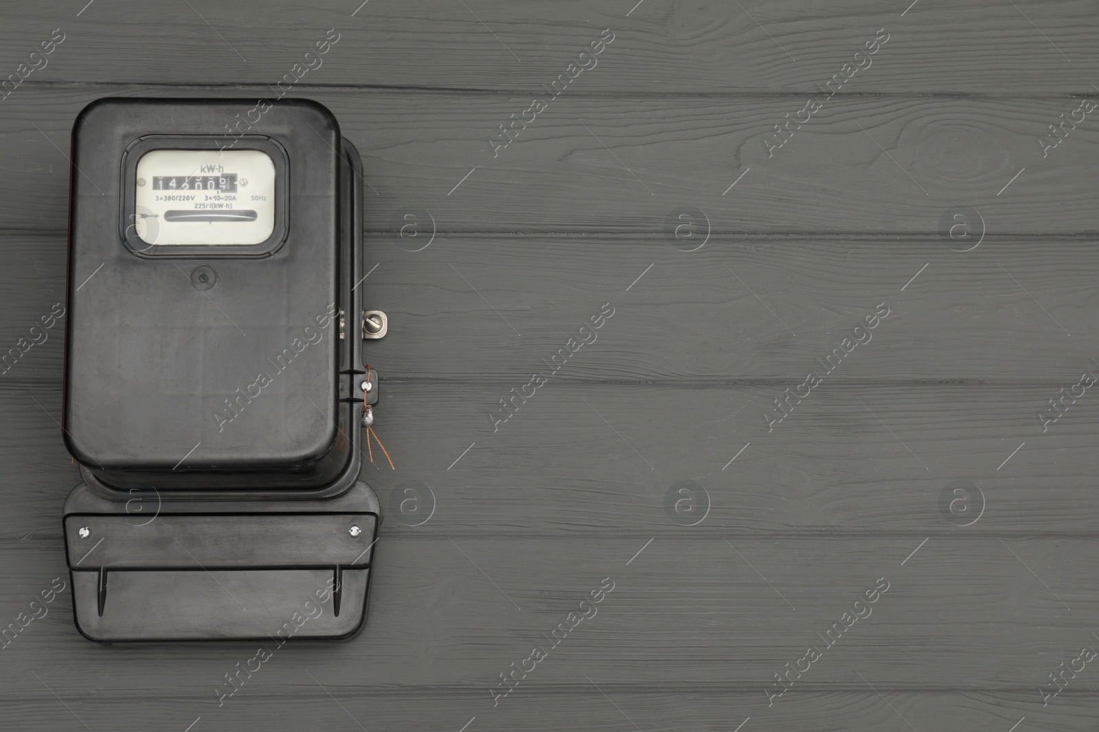 Photo of Black electric meter on grey wooden background, top view with space for text. Measuring device