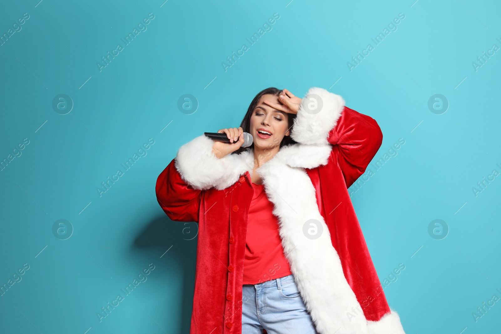 Photo of Young woman in Santa costume singing into microphone on color background. Christmas music