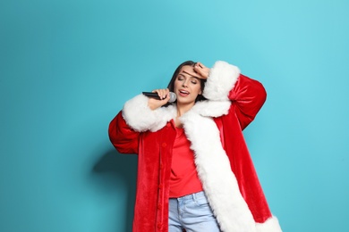 Young woman in Santa costume singing into microphone on color background. Christmas music