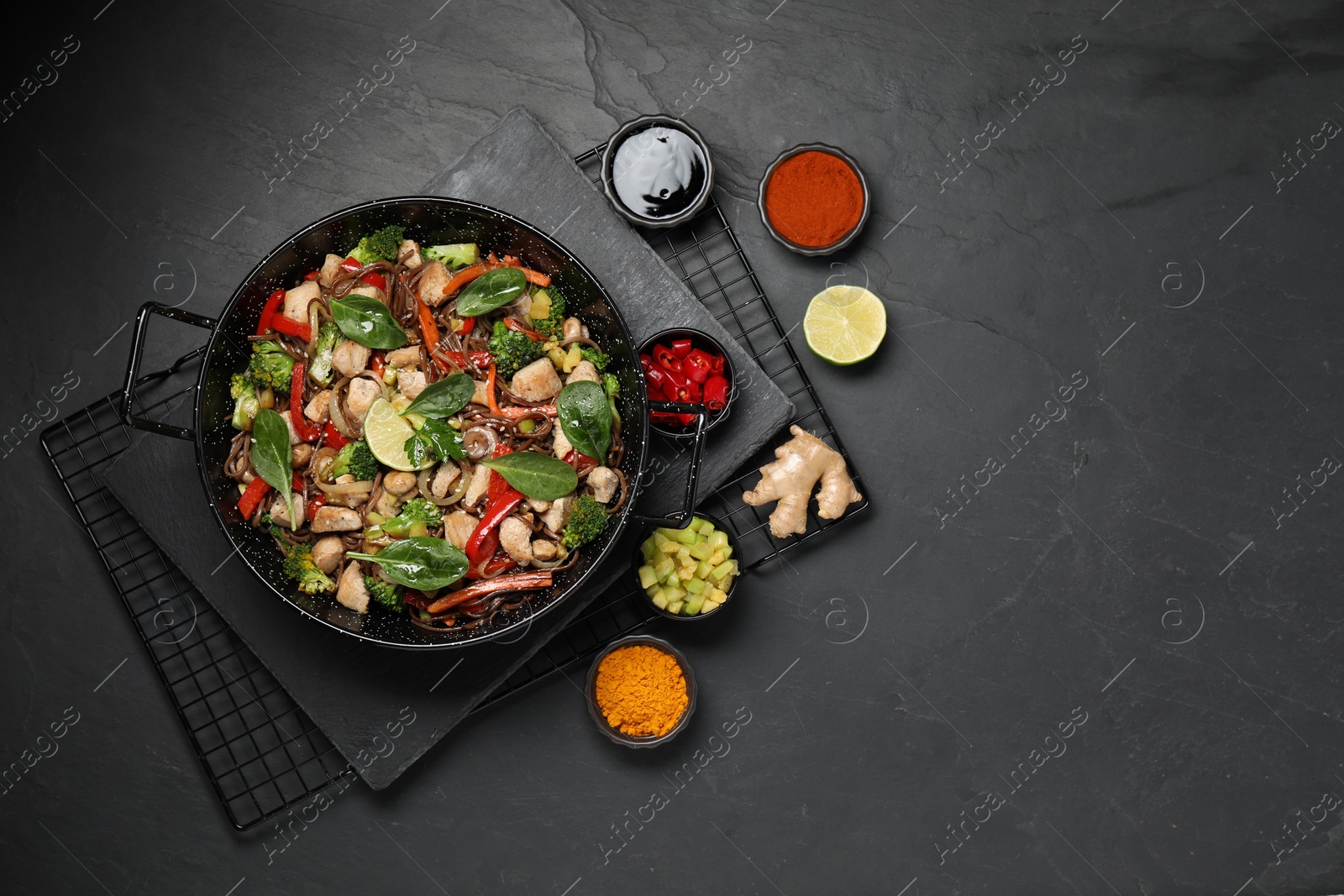 Photo of Stir-fry. Tasty noodles with meat in wok and ingredients on grey textured table, flat lay. Space for text