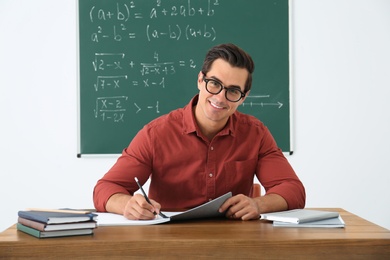 Photo of Young teacher working at table in classroom