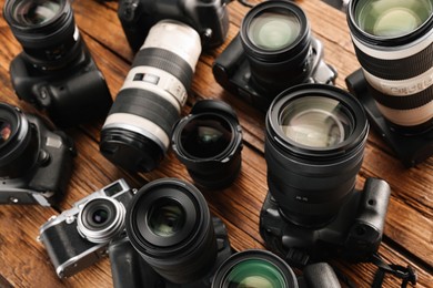 Photo of Modern cameras on wooden table, closeup. Professional photography equipment