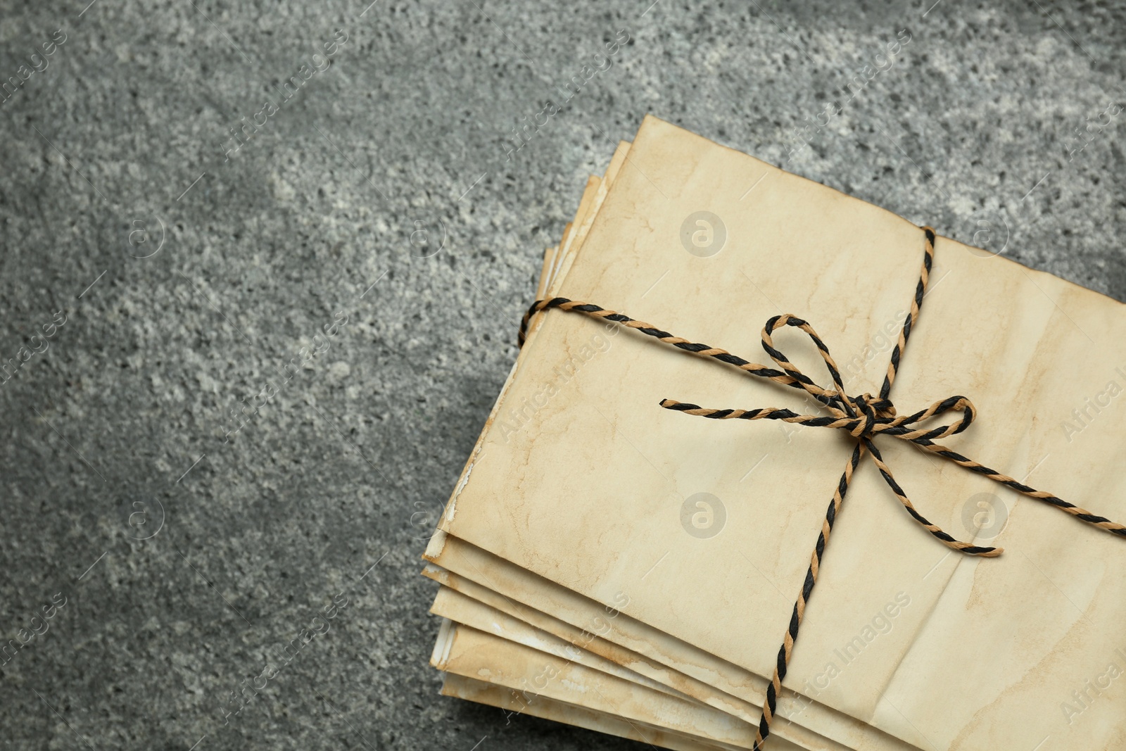 Photo of Stack of old letters tied with string on grey table, top view. Space for text