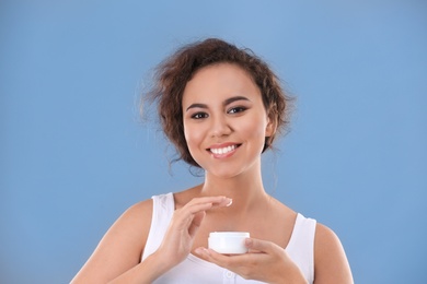 Beautiful young woman with problem skin applying anti acne cream on grey background