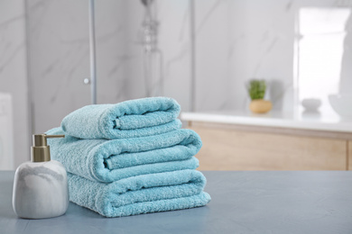 Photo of Stack of clean towels and soap dispenser on grey stone table in bathroom. Space for text