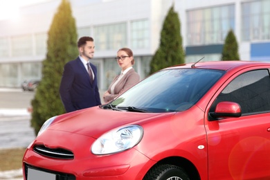 Image of Customers buying car. Modern red auto and couple, focus on new auto