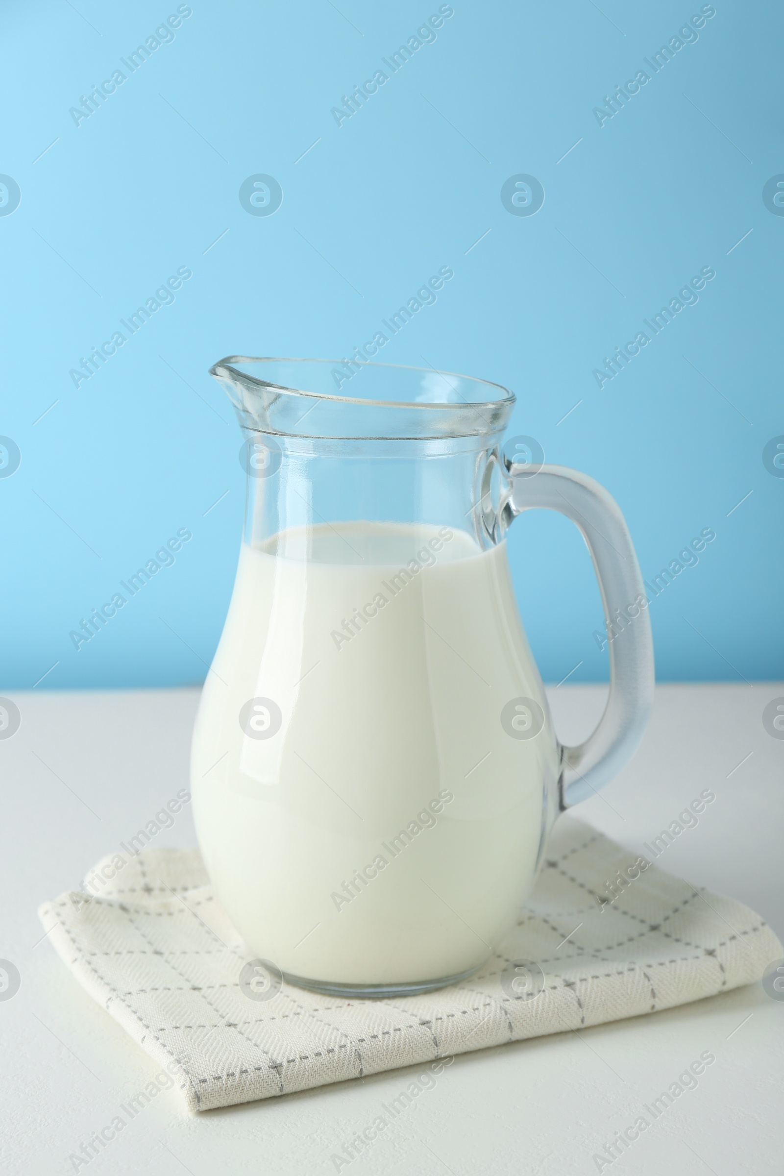 Photo of One jug of fresh milk on white table against light blue background