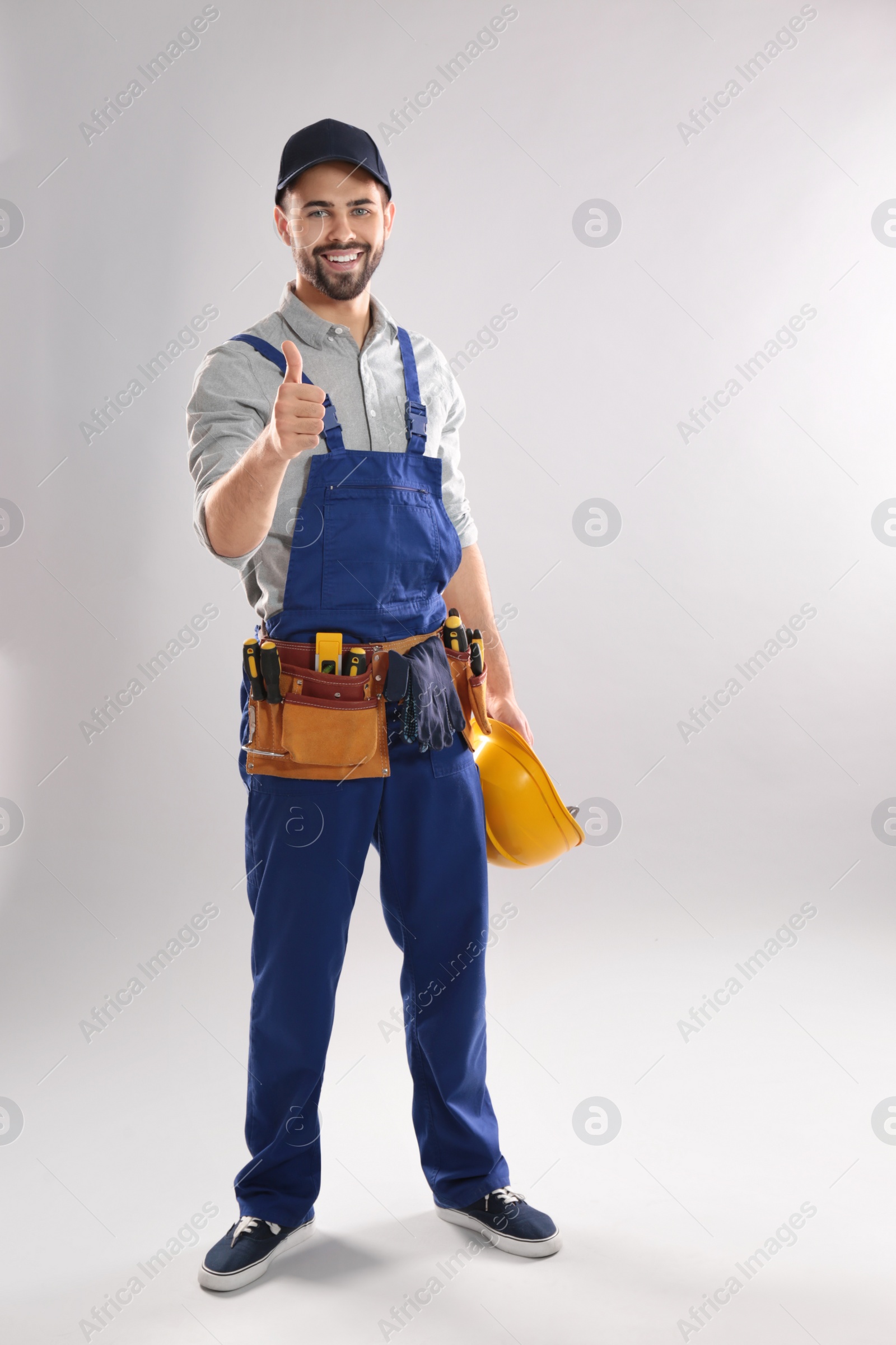 Photo of Full length portrait of construction worker with hard hat and tool belt on light background