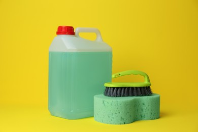 Photo of Canister of detergent, sponge and brush on yellow background. Cleaning supplies