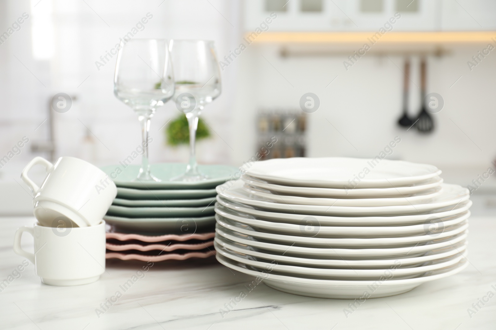 Photo of Clean plates, cups and glasses on white marble table in kitchen