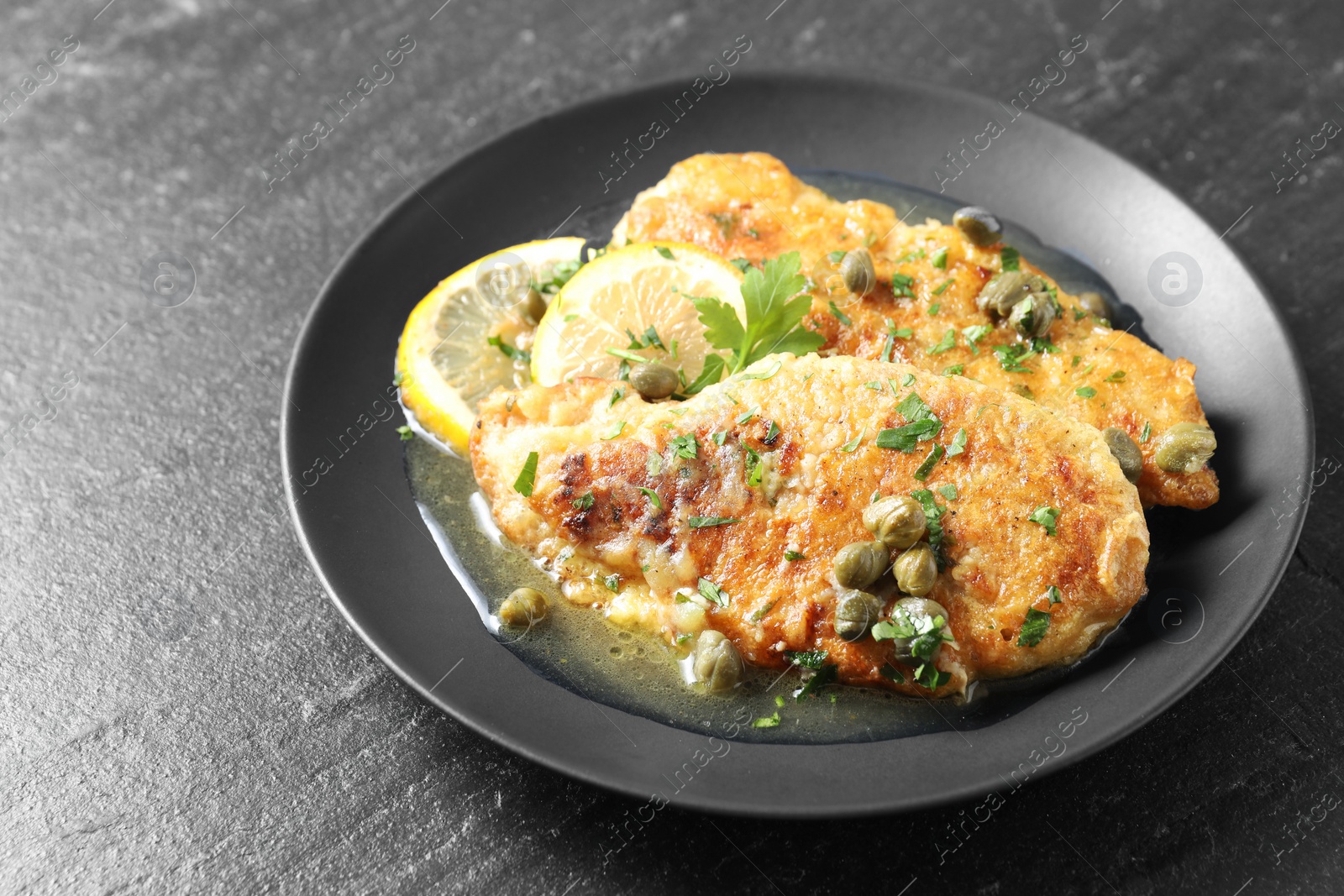 Photo of Delicious chicken piccata with herbs and lemons on black table