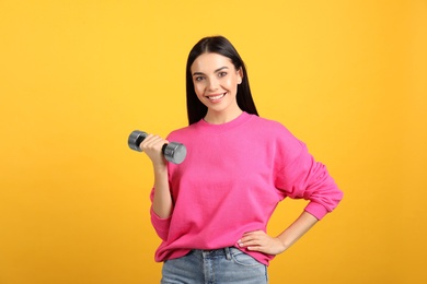 Photo of Woman with dumbbell as symbol of girl power on yellow background. 8 March concept