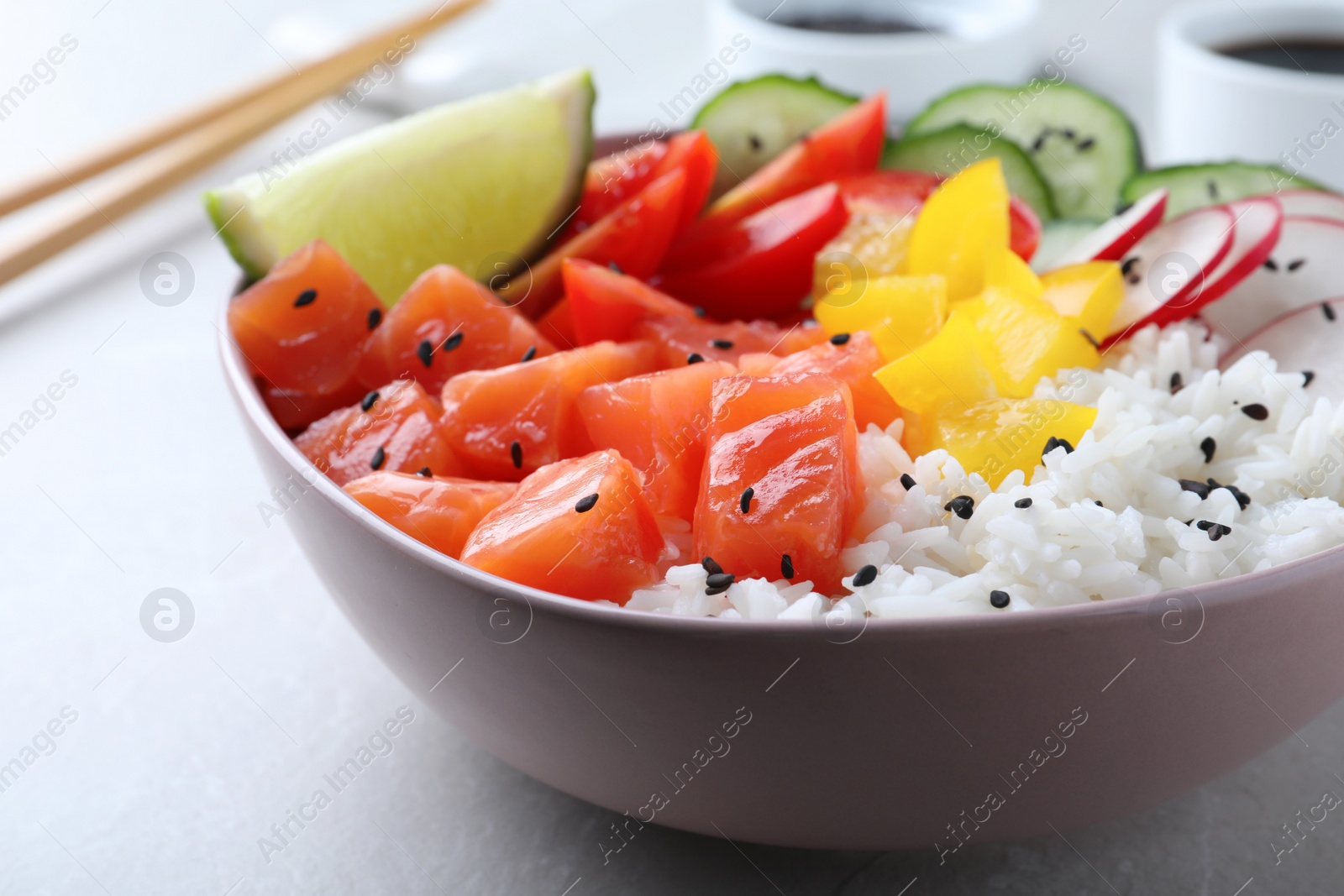 Photo of Delicious poke bowl with salmon, rice and vegetables on light grey table, closeup