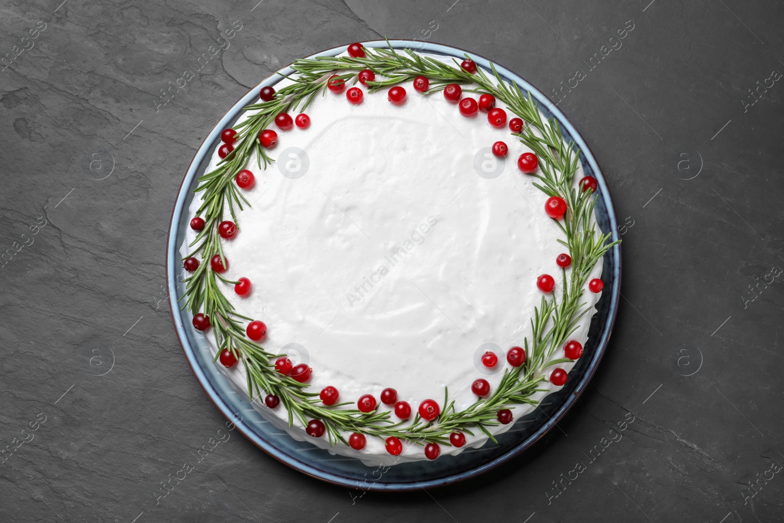 Photo of Traditional Christmas cake decorated with rosemary and cranberries on dark grey table, top view