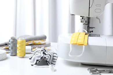 Photo of Sewing machine, homemade protective masks and craft accessories on white table