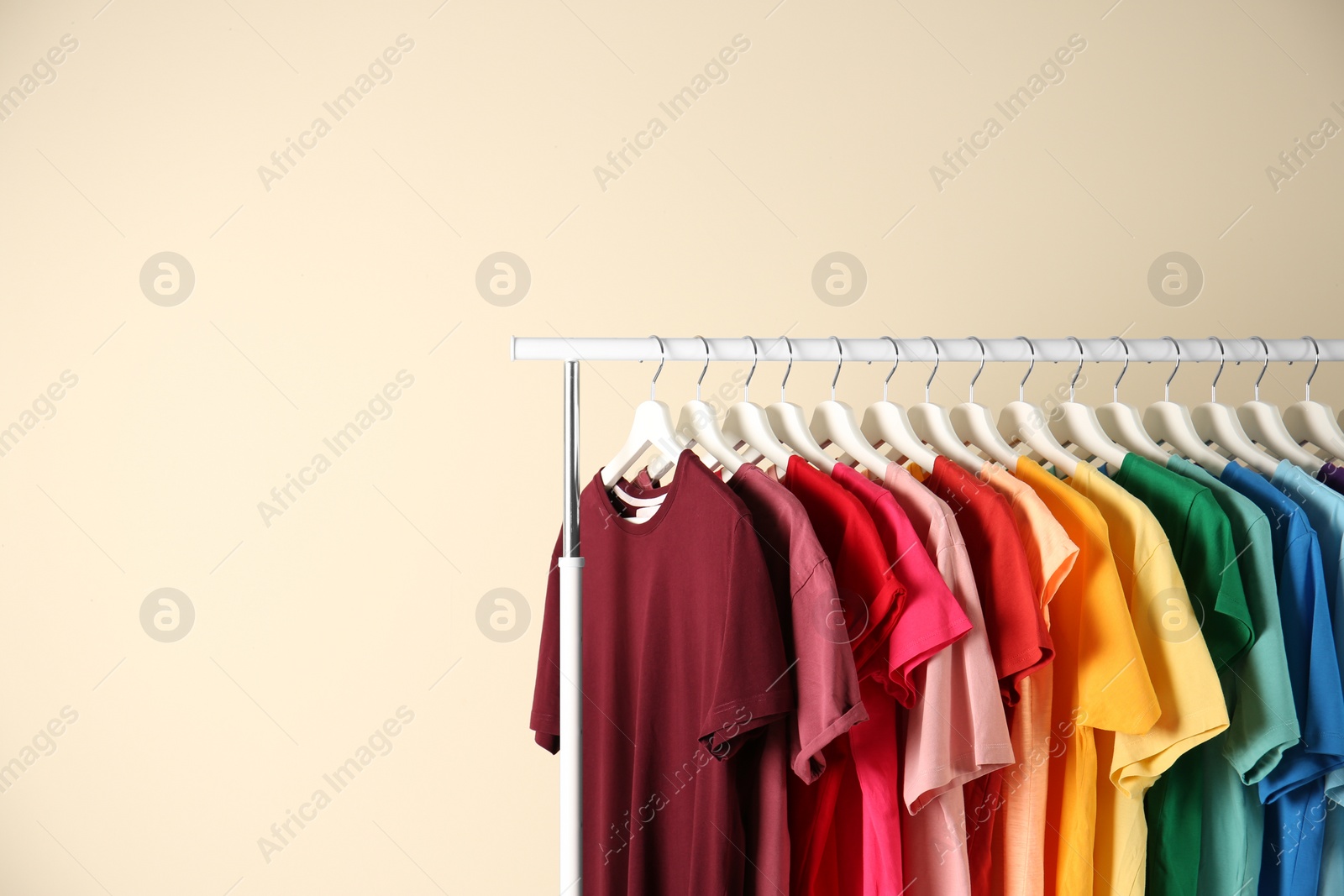 Photo of Many t-shirts hanging in order of rainbow colors on light background