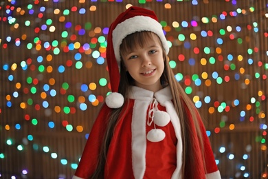 Photo of Cute little child in Santa hat on blurred lights background. Christmas celebration