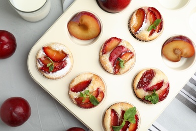 Delicious cupcakes with plums in baking pan, flat lay