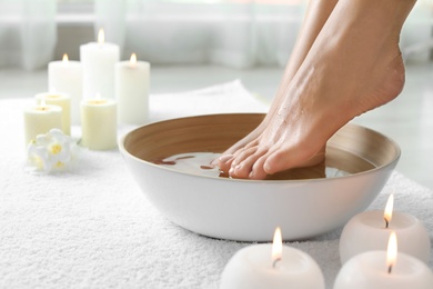 Photo of Woman soaking her feet in dish indoors, closeup with space for text. Spa treatment