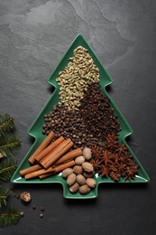 Photo of Different spices, nuts and fir branches on dark gray textured table, flat lay