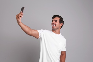 Photo of Handsome young man taking selfie with smartphone on grey background