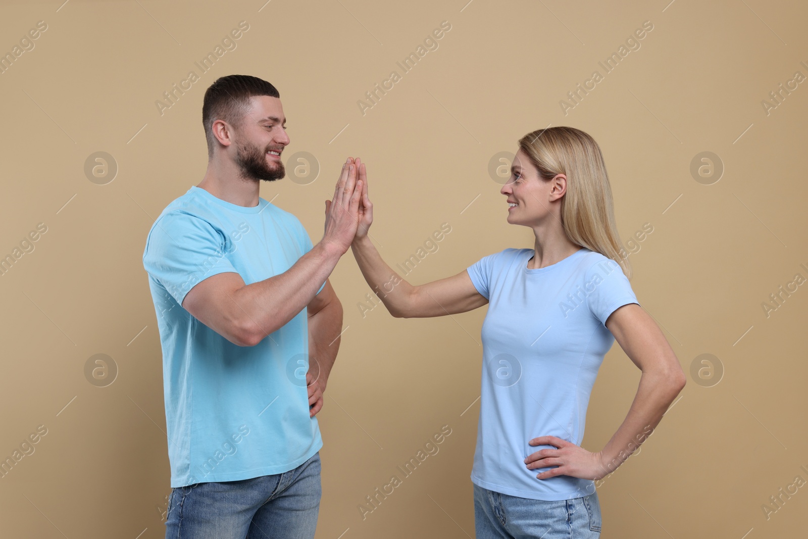 Photo of Happy couple giving high five on light brown background