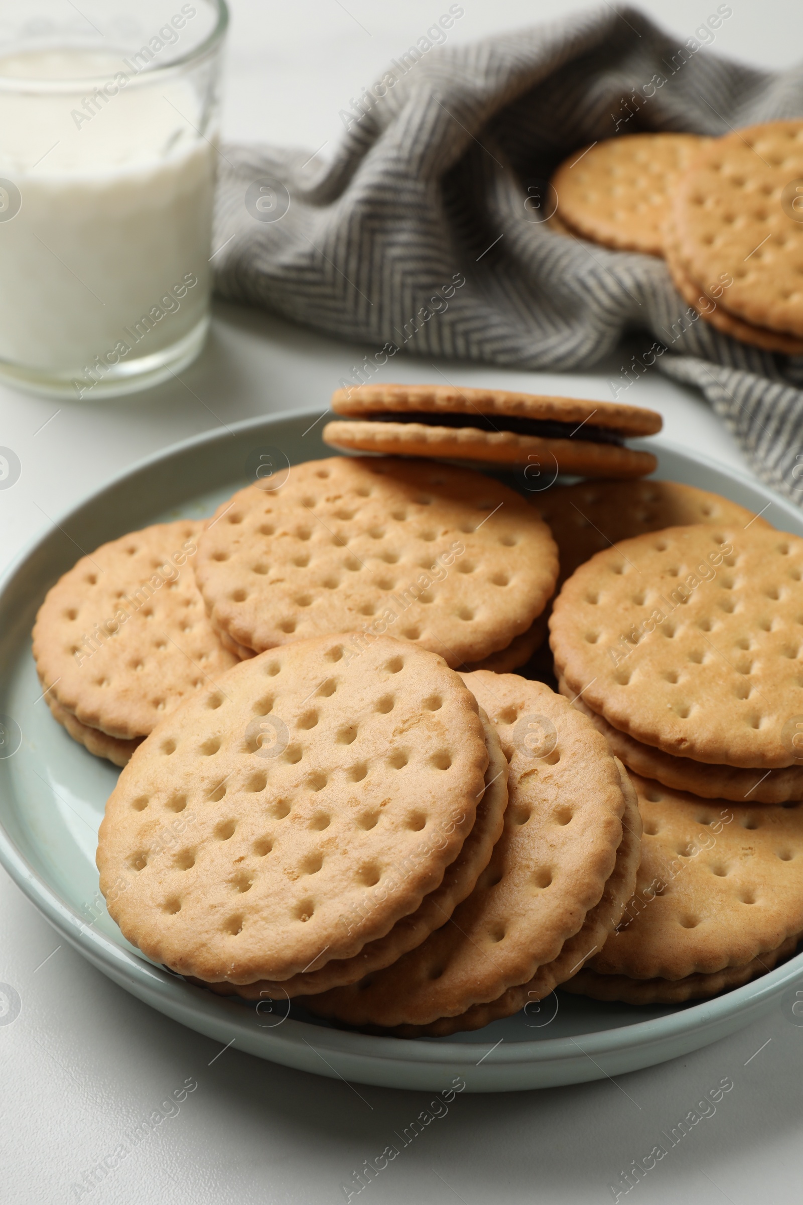 Photo of Tasty sandwich cookies and glass of milk on white table, closeup