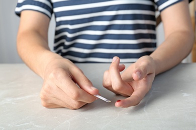 Photo of Woman with blood sugar test stripe at table. Diabetes control