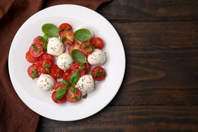 Tasty salad Caprese with tomatoes, mozzarella balls and basil on wooden table, top view. Space for text