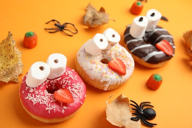Photo of Delicious donuts decorated as monsters on orange background. Halloween treat