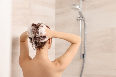 Photo of Young woman washing her hair with shampoo in shower, back view. Space for text