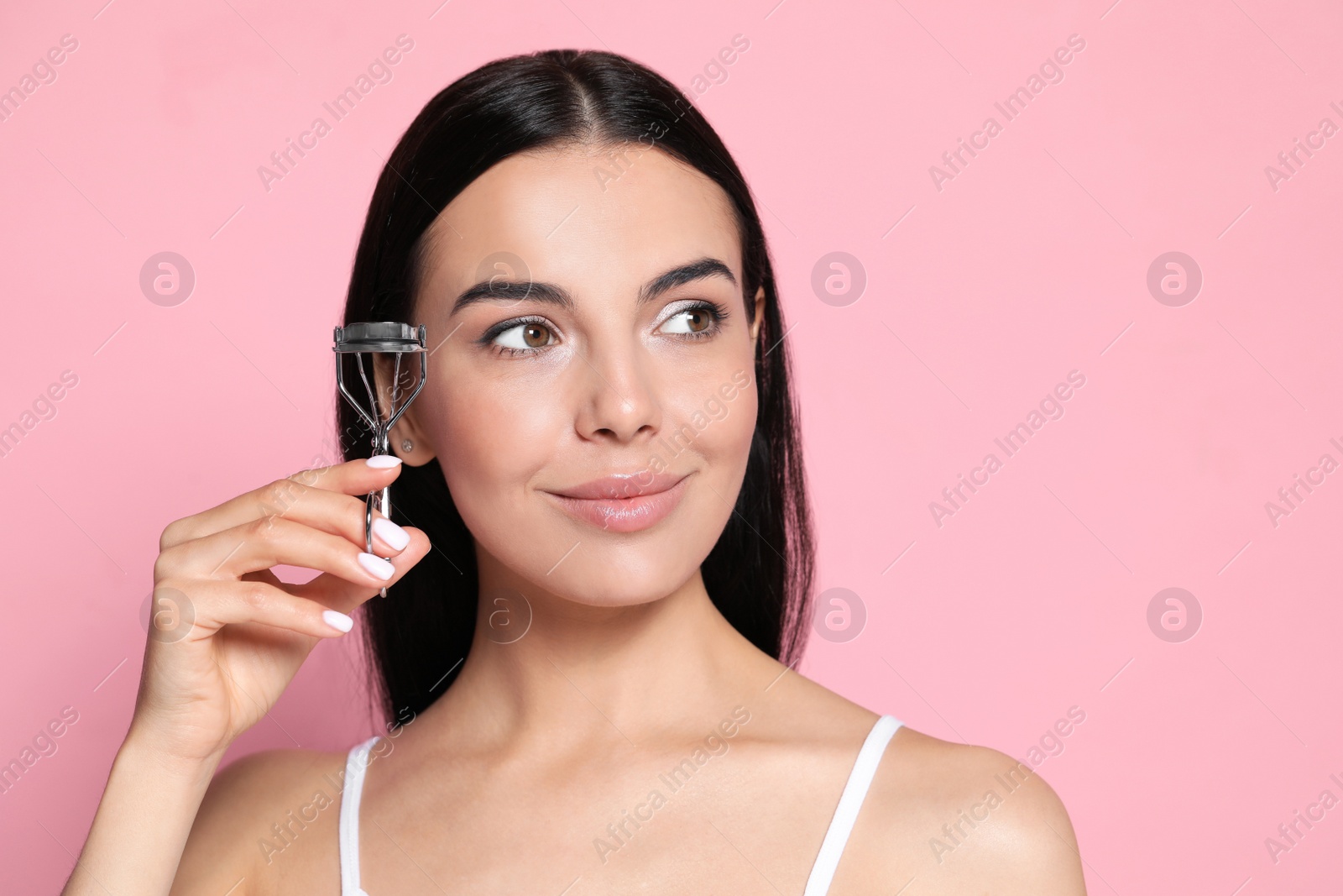 Photo of Beautiful young woman with eyelash curler on light pink background, space for text
