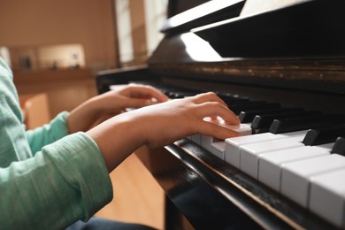 Photo of Little child playing piano indoors, closeup. Music lesson