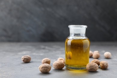 Photo of Bottle of nutmeg oil and nuts on grey table, space for text