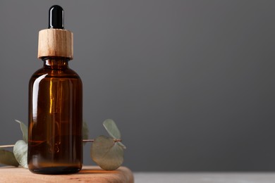 Photo of Bottle of face serum and leaves on wooden stand against grey background, closeup. Space for text