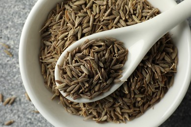 Photo of Caraway (Persian cumin) seeds and spoon in bowl on gray table, top view