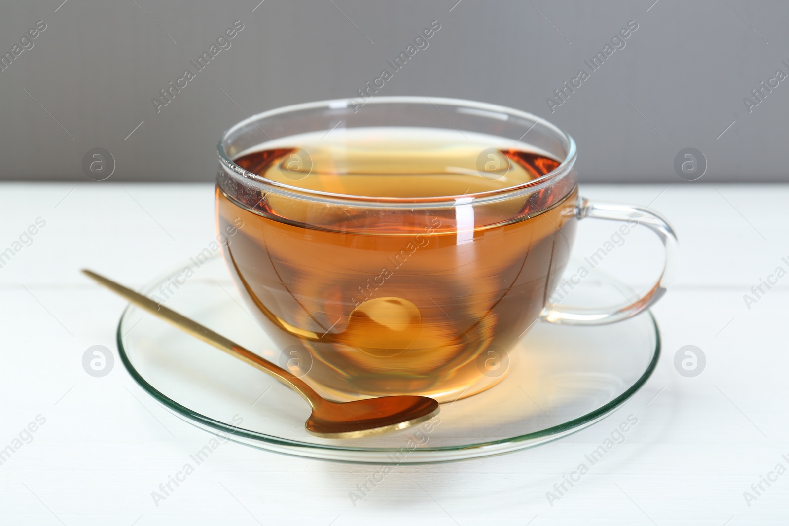 Photo of Glass cup of tea and spoon on white table