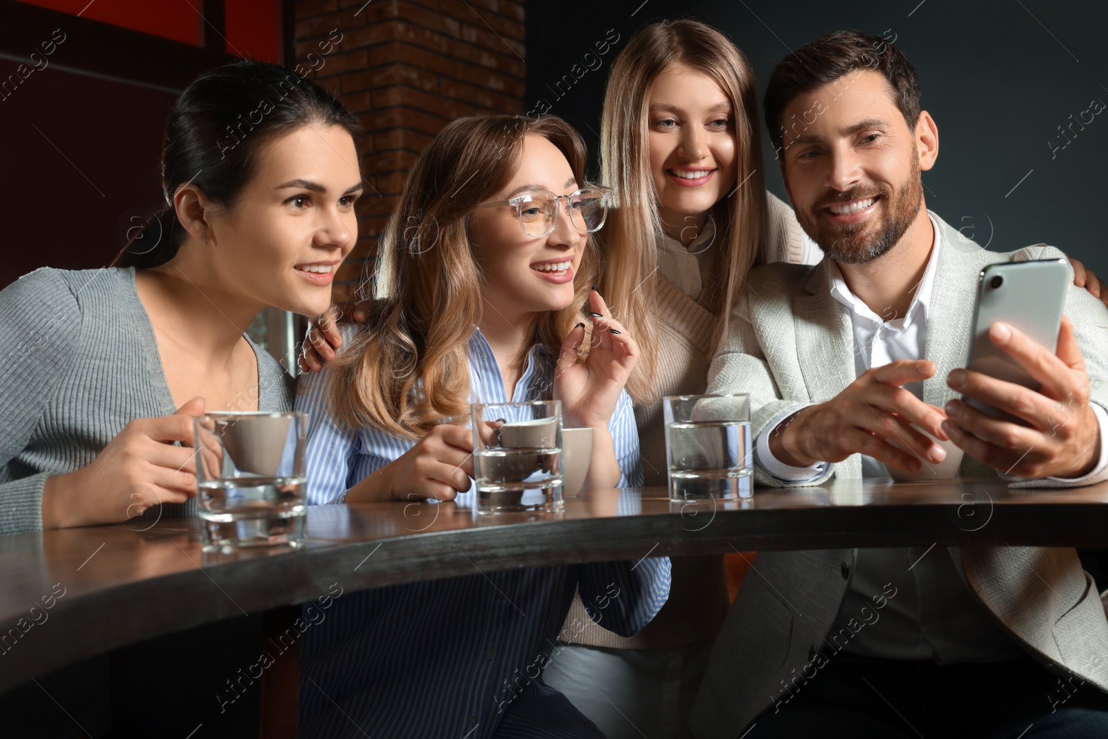 Photo of Handsome man showing something funny in smartphone to his friends in cafe