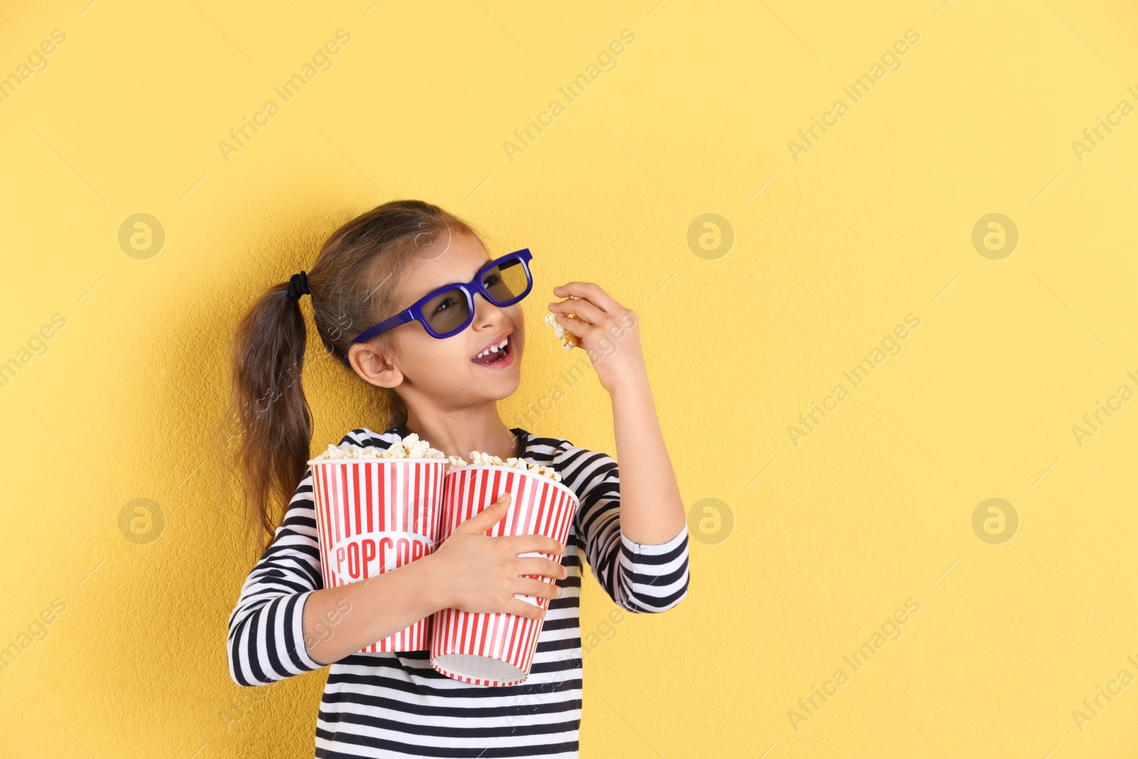 Photo of Cute little girl with popcorn and glasses on color background. Space for text