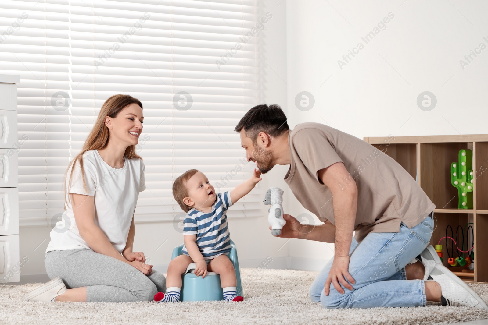 Photo of Parents training their child to sit on baby potty indoors