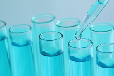 Dripping liquid from pipette into test tube on blurred background, closeup. Laboratory analysis