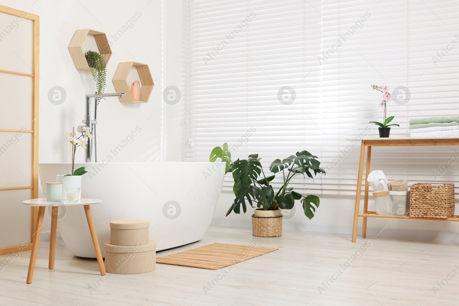 Photo of Stylish bathroom interior with bath tub, houseplants and bamboo mat