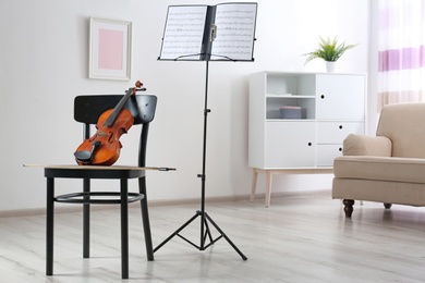 Violin, chair and note stand with music sheets in room