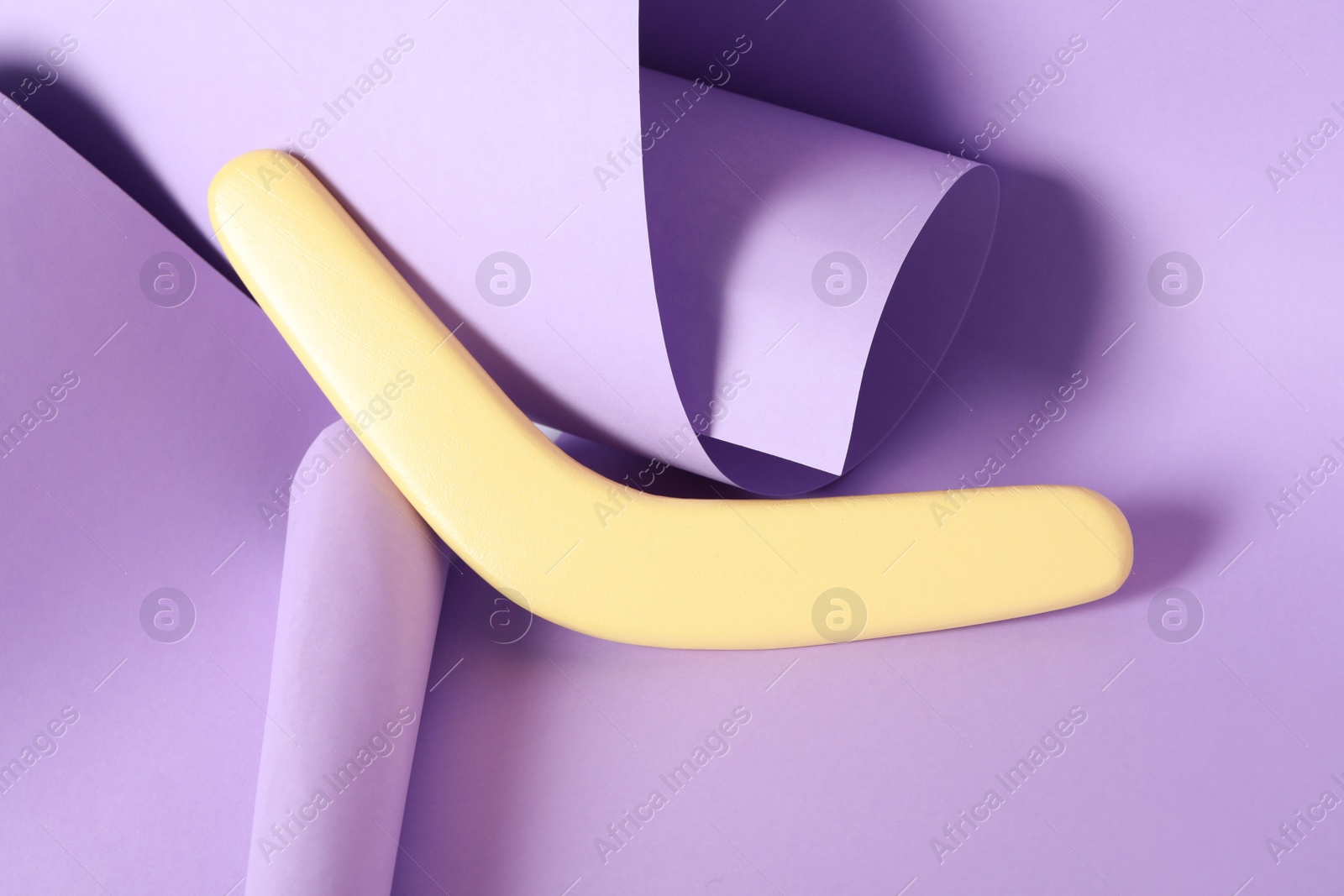 Photo of Creative composition with yellow wooden boomerang on lilac background