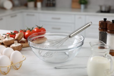 Photo of Whisk, bowl, and different ingredients on white marble table indoors