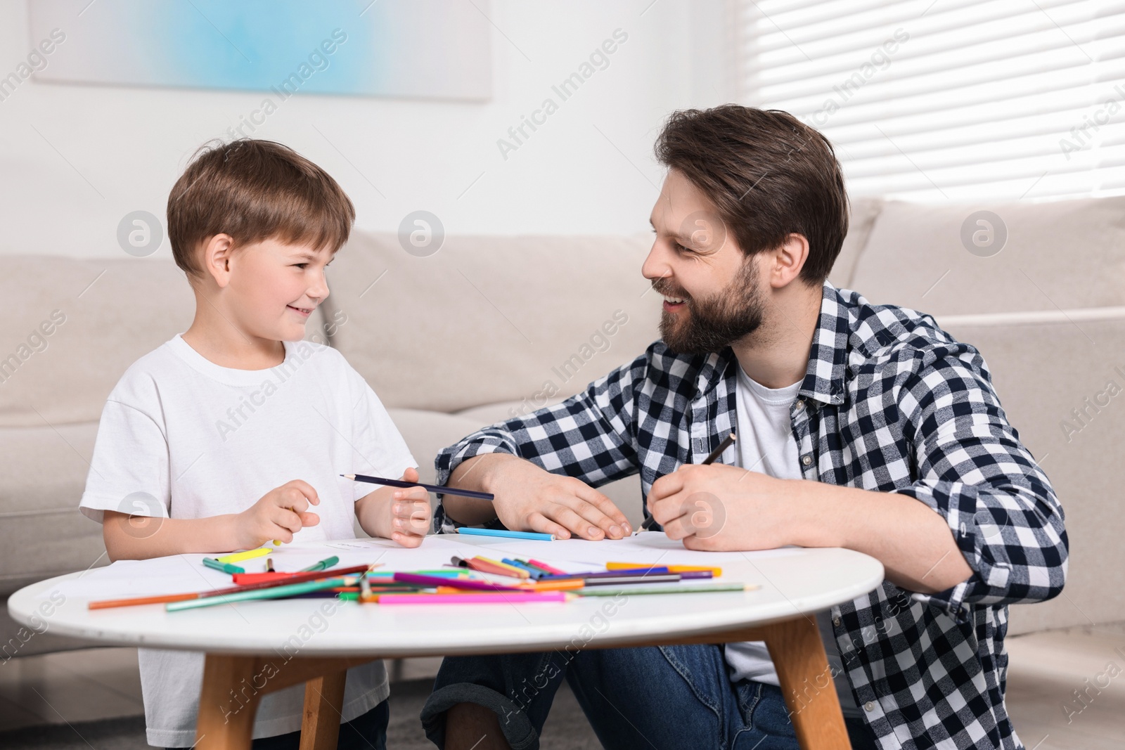 Photo of Dad and son drawing together at coffee table indoors