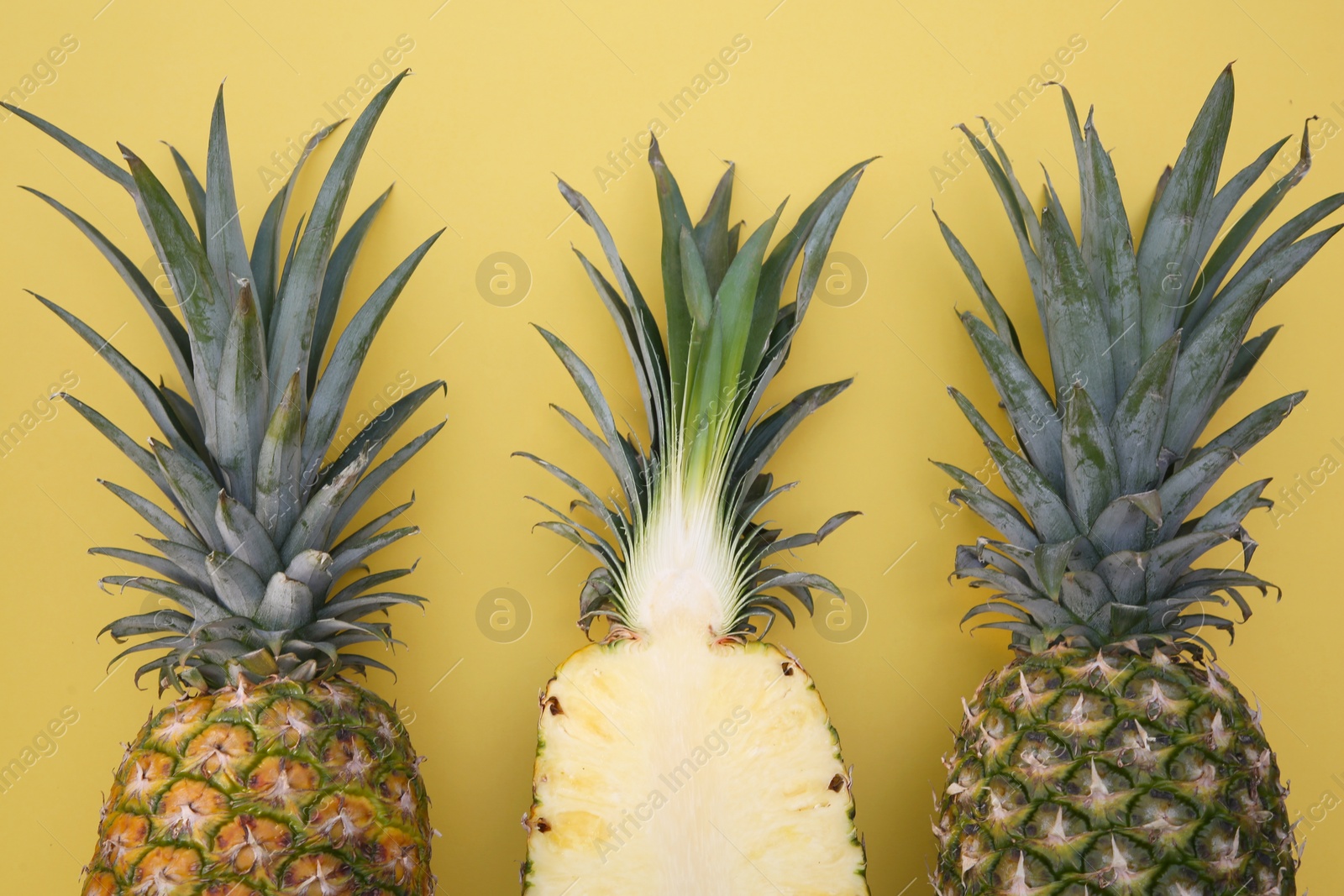Photo of Whole and cut ripe pineapples on yellow background, flat lay